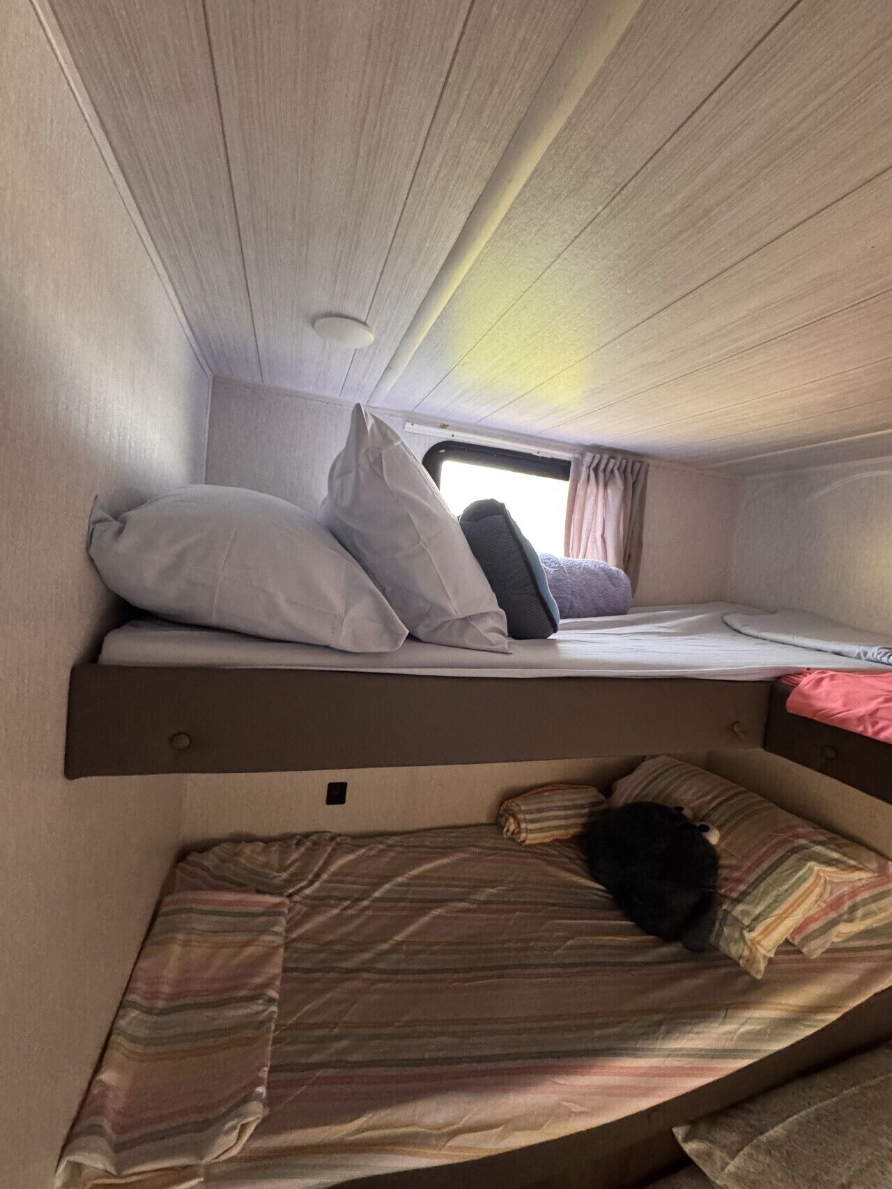 A compact RV interior with a bunk bed and a lower sleeping area.