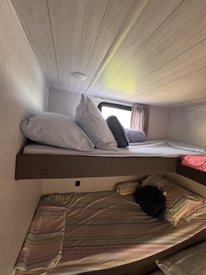 A compact RV interior with a bunk bed and a lower sleeping area.