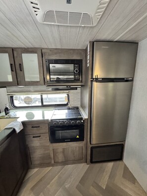 A compact kitchenette with a microwave, stove, and refrigerator.