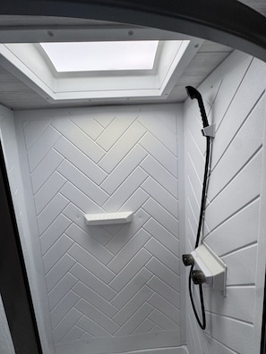 A compact shower area with a herringbone-patterned wall, a built-in shelf, and a handheld showerhead.