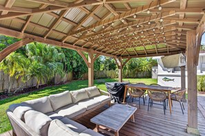 A covered outdoor patio with a wooden ceiling, a sofa, a table, and chairs. - The Oasis Private Pool +Gazebo 5 Minutes to the Beach! (Pompano Beach)