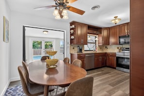 A modern kitchen with wooden cabinets, a dining table, and a ceiling fan. - The Oasis Private Pool +Gazebo 5 Minutes to the Beach! (Pompano Beach)