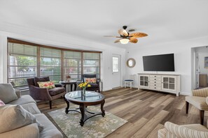 A living room with a large window, a ceiling fan, a flat-screen TV, and a wooden cabinet. - The Oasis Private Pool +Gazebo 5 Minutes to the Beach! (Pompano Beach)