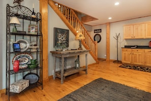 A wooden staircase leading to a loft area with a rustic decor, including a wooden table, shelves with various items, and a painting of an owl.