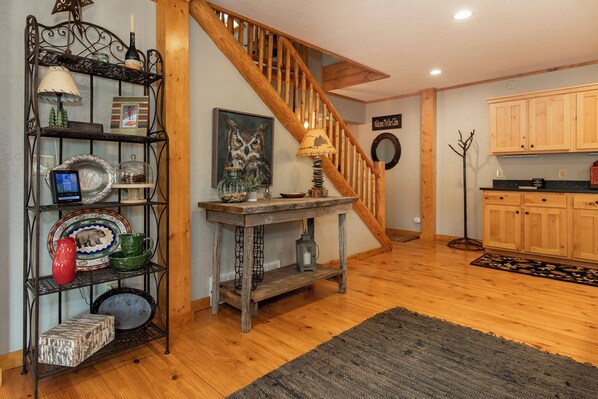 A wooden staircase leading to a loft area with a rustic decor, including a wooden table, shelves with various items, and a painting of an owl.