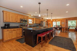 A kitchen with wooden cabinets, stainless steel appliances, a central island with stools, and a dining area with chairs.