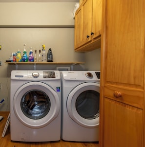 A laundry room with two front-loading washing machines and a shelf with various cleaning products.