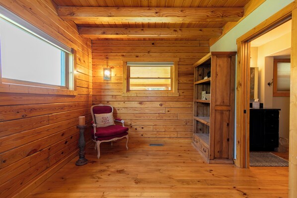 A wooden cabin interior with a chair, a shelf, and a window.