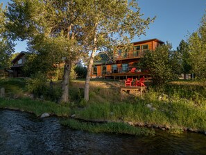 A cabin with a deck, surrounded by trees and a stream.