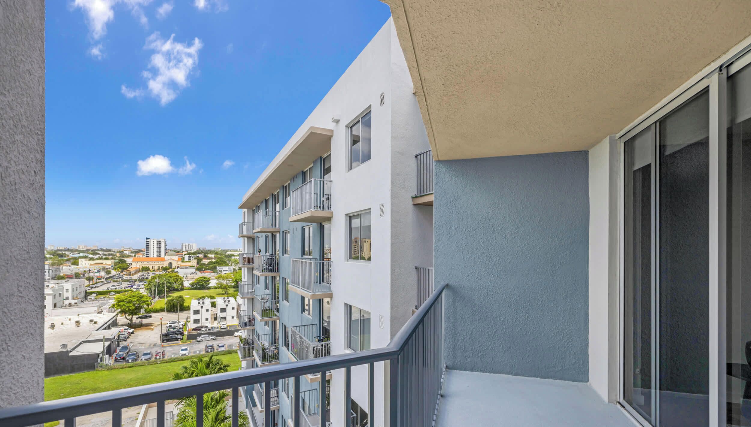 Ein Balkon mit Blick auf eine Stadtlandschaft, mit mehrstöckigen Gebäuden und blauem Himmel.