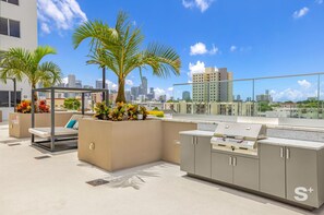 A rooftop bar with a grill, seating area, and palm trees. - Modern Miami 1BR - Pool - Gym - Parking - Balcony (Miami)