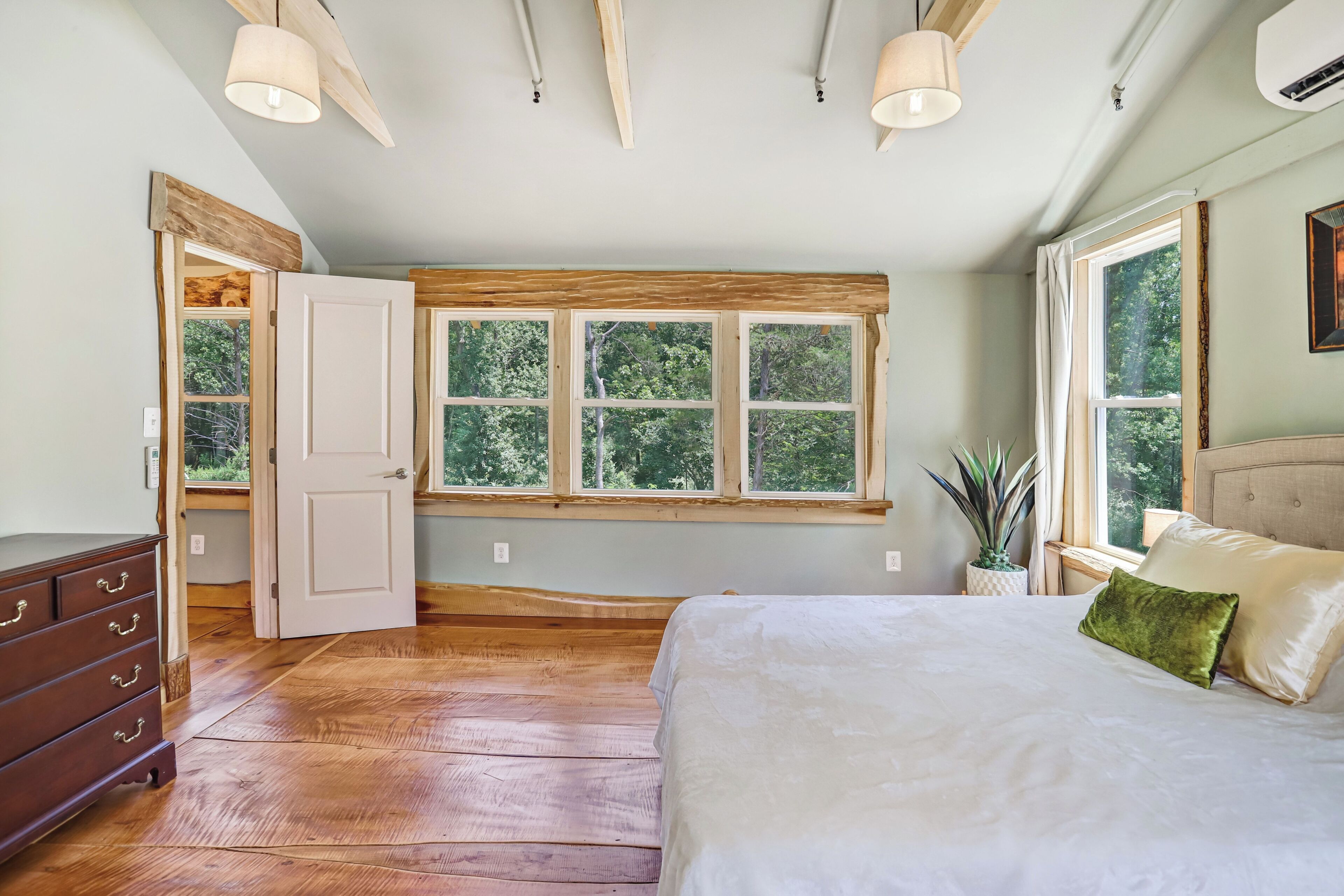 A bedroom with a large bed, a window with multiple panes, a wooden floor, and a dresser.