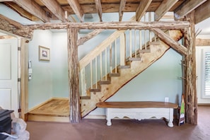A rustic wooden staircase with a bench at the bottom, a door on the left, and a wall-mounted picture.