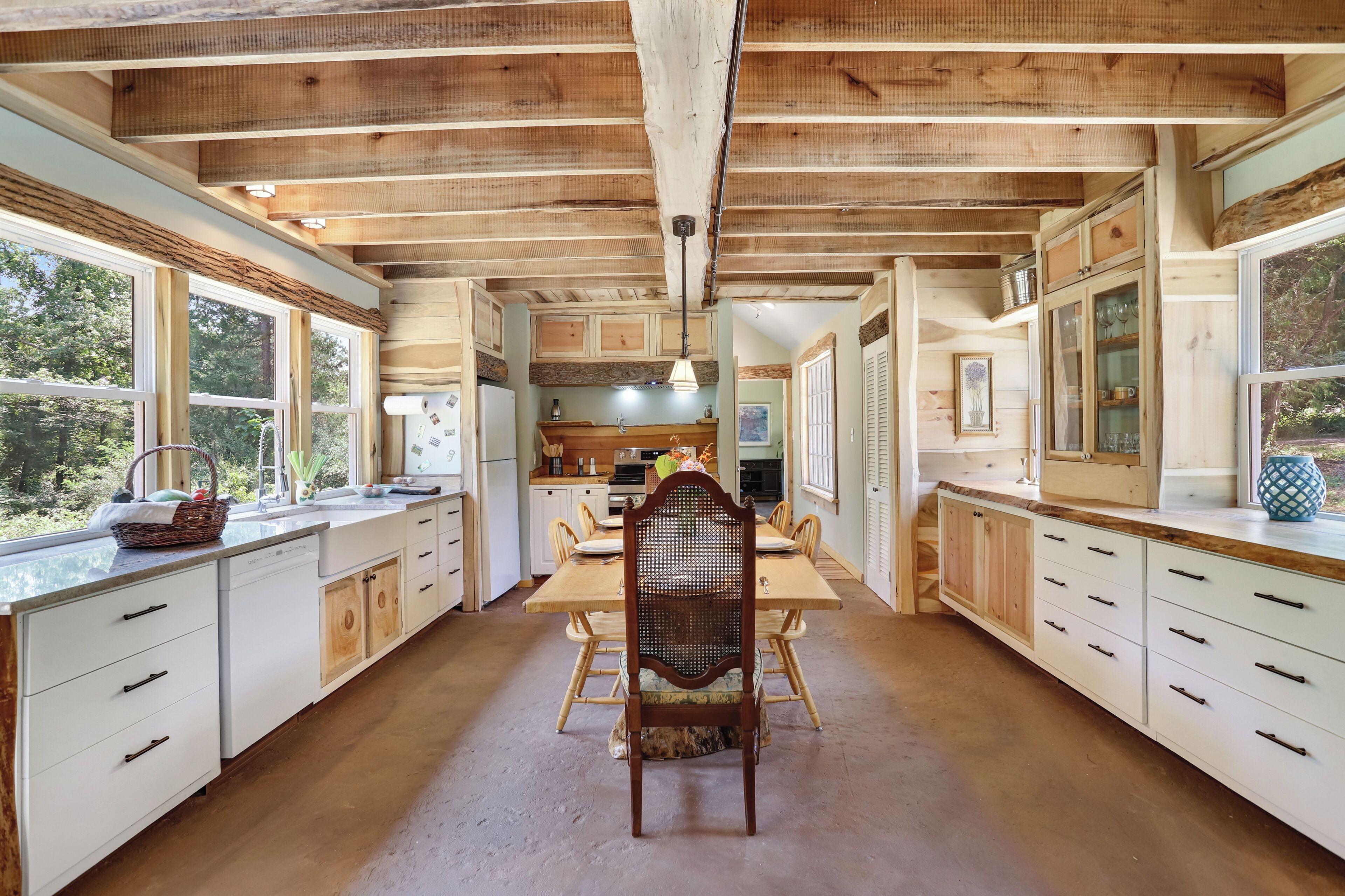 Un interior de madera con una mesa de comedor, sillas, armarios de cocina y un ventanal grande.