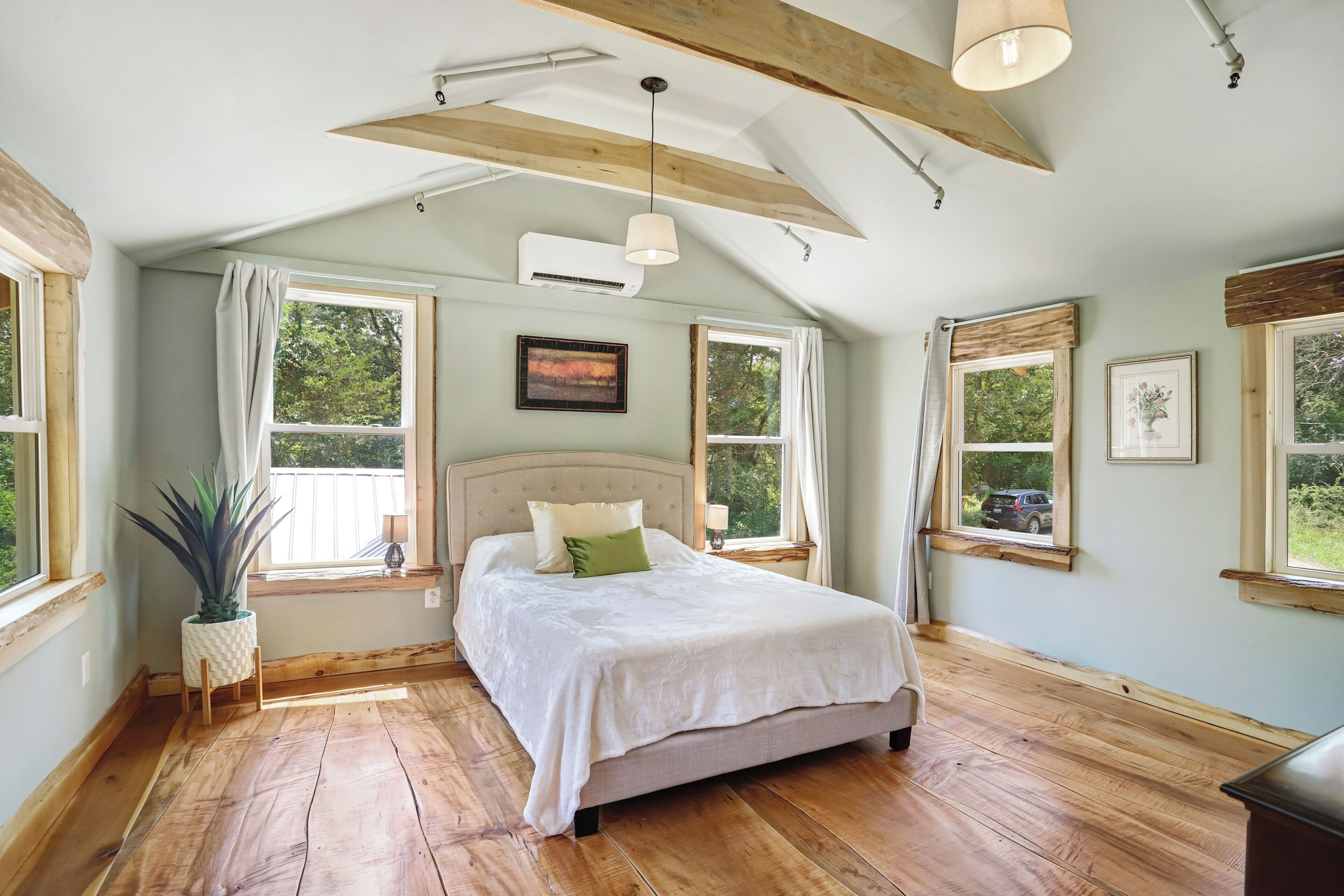 A bedroom with a bed, wooden beams, a ceiling fan, and large windows.