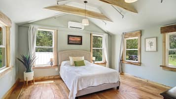 A bedroom with a bed, wooden beams, a ceiling fan, and large windows.