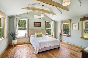 A bedroom with a bed, wooden beams, a ceiling fan, and large windows.