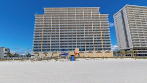 Ein großes Hotel mit mehreren Etagen, ein Strand im Vordergrund und ein klarer, blauer Himmel.