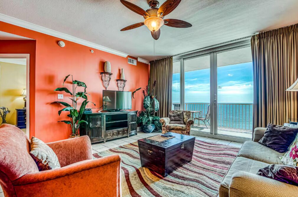 A living room with a large window, a ceiling fan, and a view of the ocean.