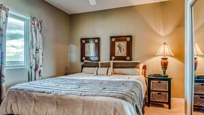 A bedroom with a bed, a ceiling fan, a window with curtains, and a nightstand with a lamp.