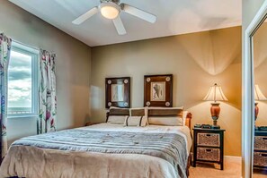 A bedroom with a bed, a ceiling fan, a window with curtains, and a nightstand with a lamp. - San Carlos 1208 | Beach Front (Gulf Shores)