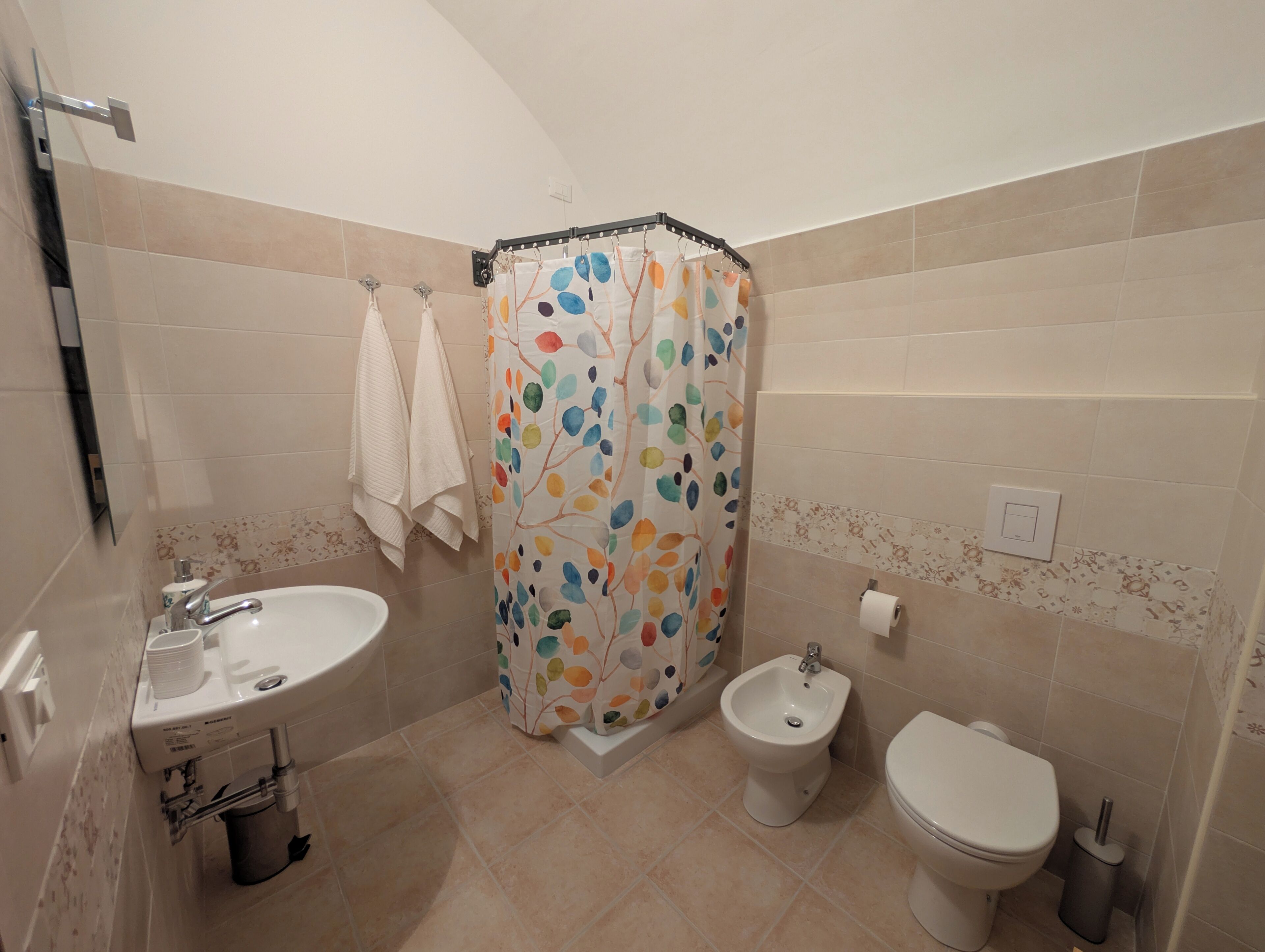 A bathroom with a sink, bidet, toilet, and a shower curtain with a leaf pattern.