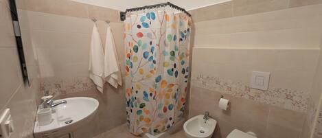 A bathroom with a sink, bidet, toilet, and a shower curtain with a leaf pattern.