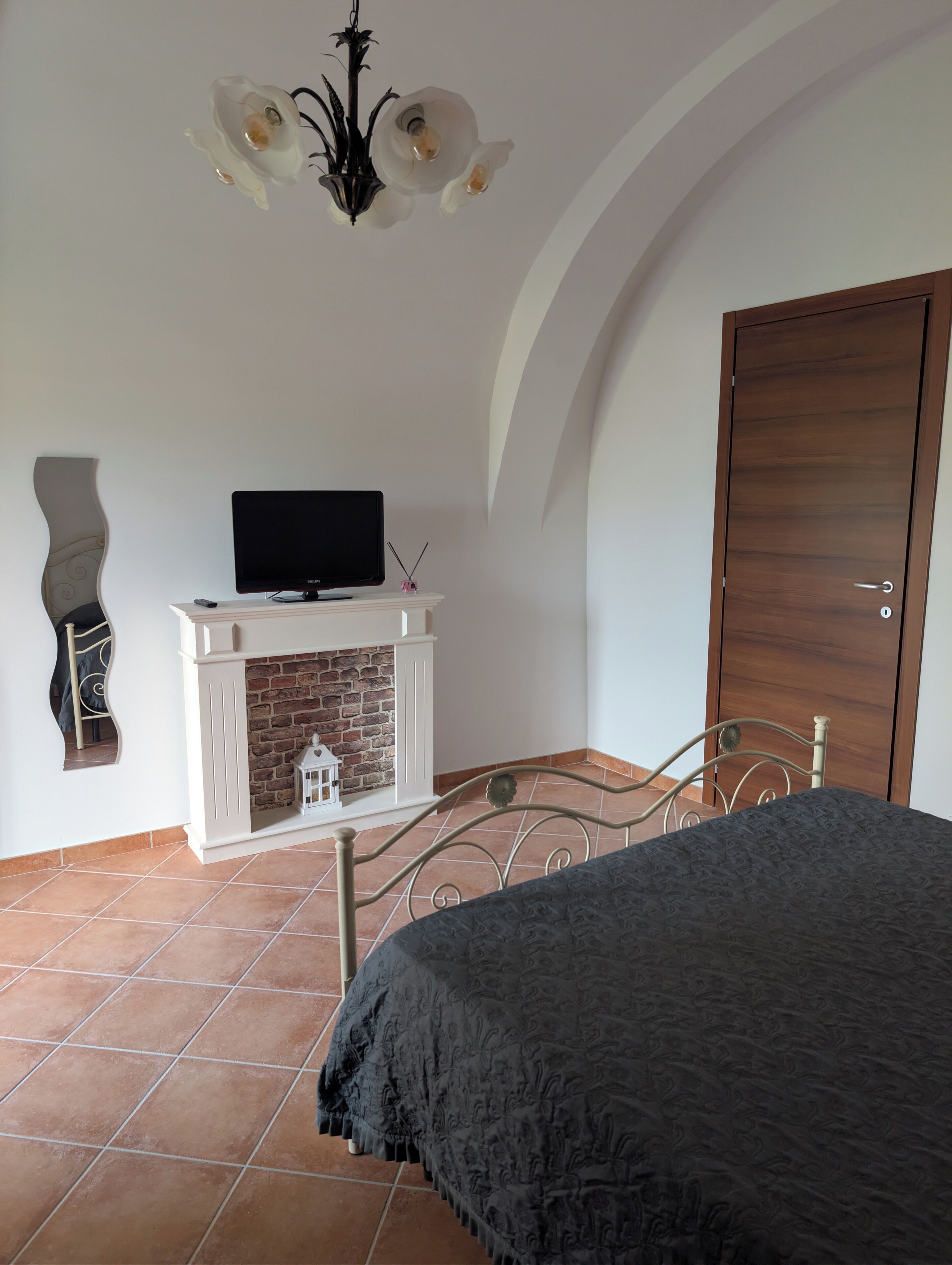 Una camera da letto con un letto, una televisione su un camino in legno bianco, un caminetto, una porta in legno e un lampadario.