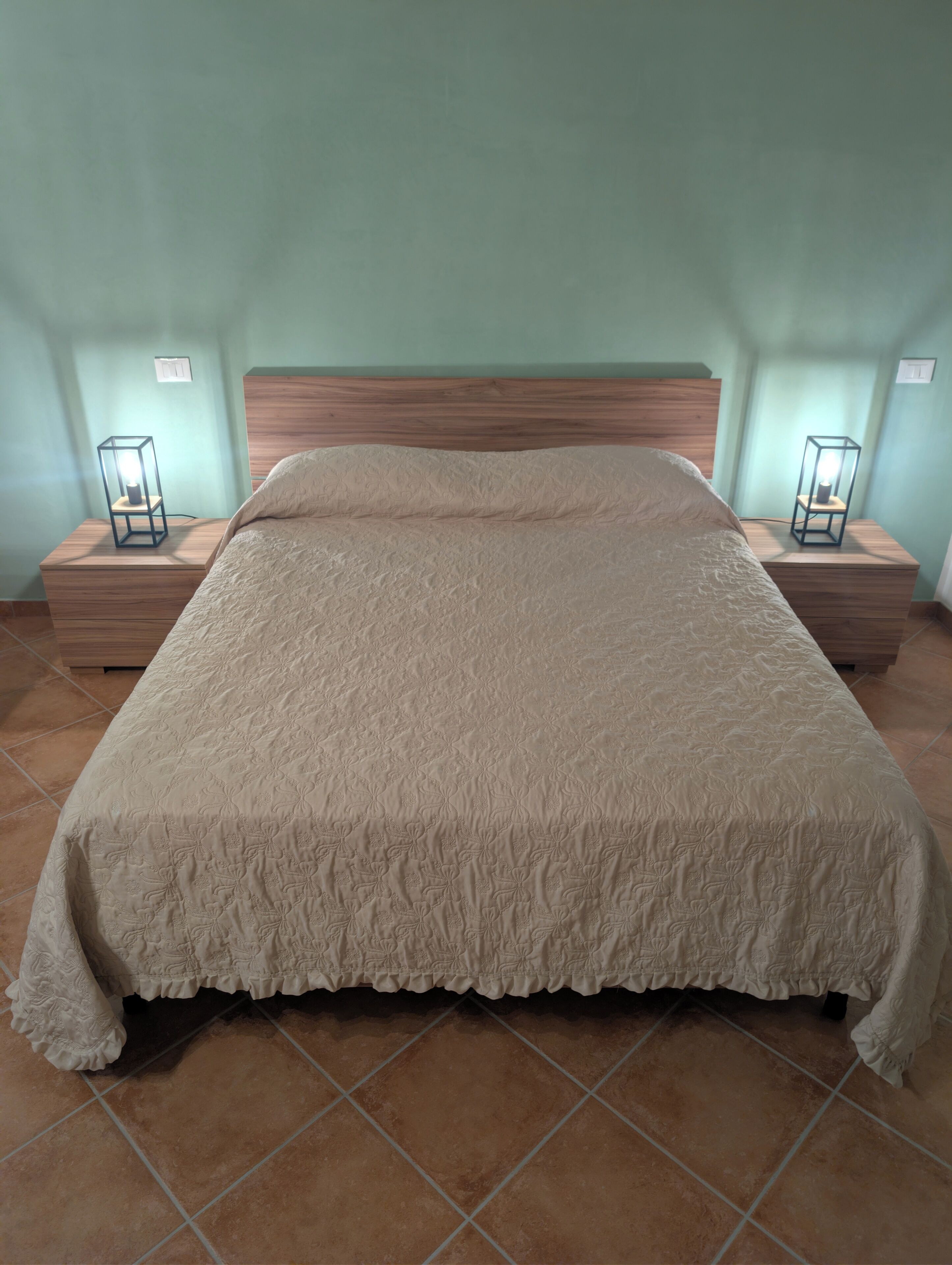 A bed with a textured blanket, wooden headboard, and two bedside tables with lamps.
