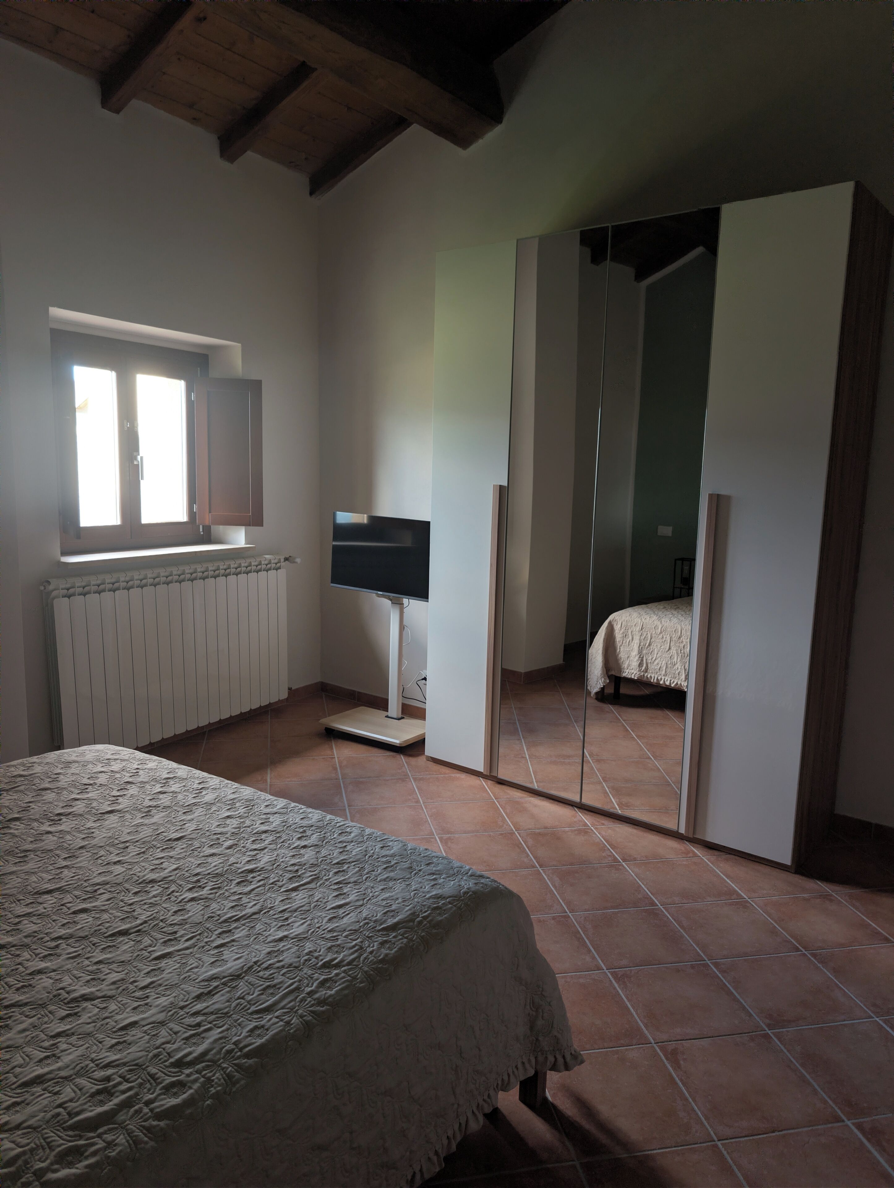 A bedroom with a bed, a TV, a window, and a wardrobe.