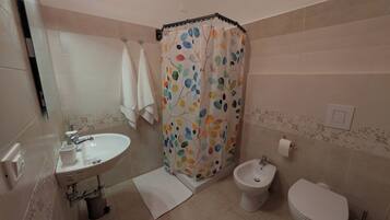 Een badkamer met een wastafel, bidet, toilet en een douchegordijn met een kleurrijk bladmotief.