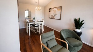 Un coin repas avec une table et des chaises blanches, un lustre et un tableau au mur.