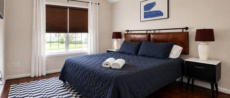 A bedroom with a bed, nightstands, a ceiling fan, a window with curtains, and a patterned rug.