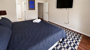 Une chambre à coucher avec un lit, un ventilateur de plafond, un téléviseur fixé au mur et un tapis à carreaux.