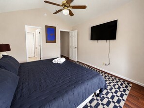 Ein Schlafzimmer mit einem Bett, einem Deckenventilator, einem an der Wand montierten Fernseher und einem Schachbrettteppich.
