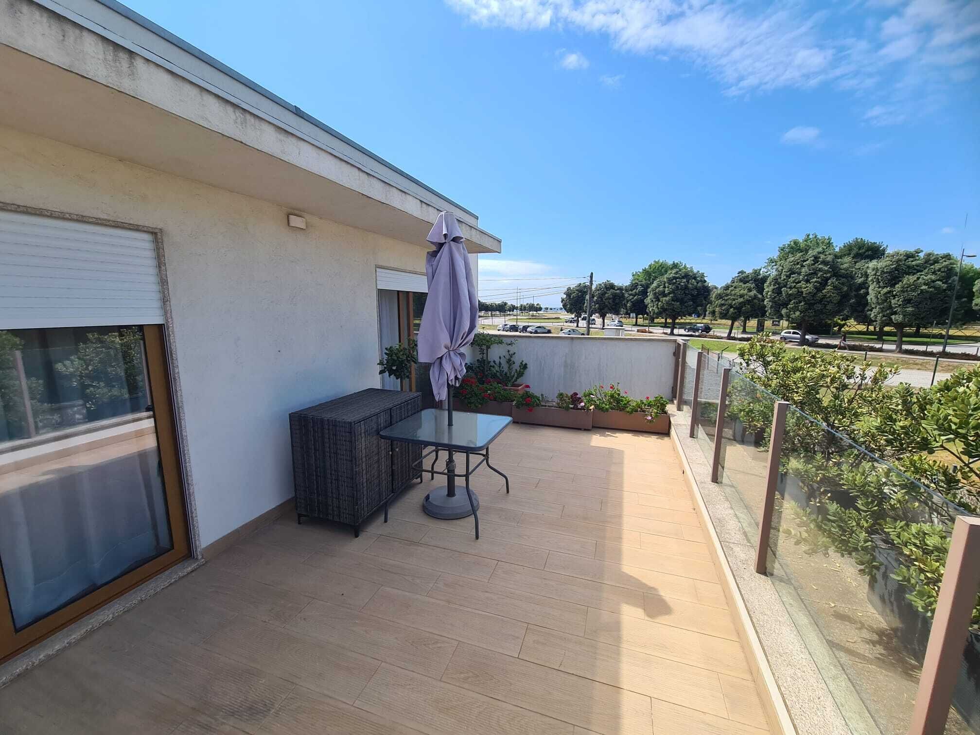 Un balcon avec une table et des chaises, un espace couvert et une vue sur la rue et les arbres.