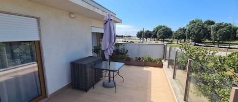 Un balcon avec une table et des chaises, un espace couvert et une vue sur la rue et les arbres.