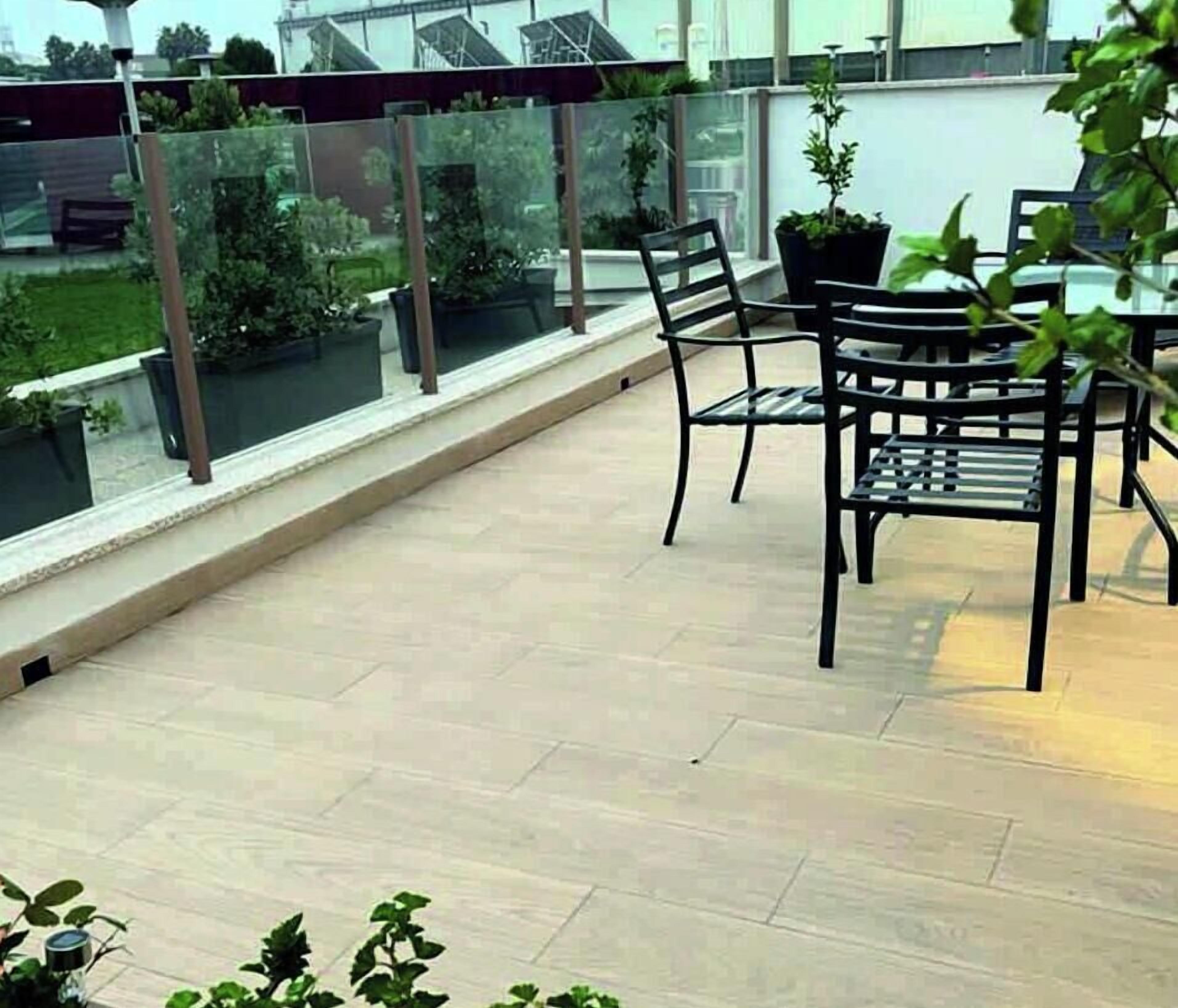 Un balcon doté d’une balustrade en verre, de deux chaises et de plantes en pot.