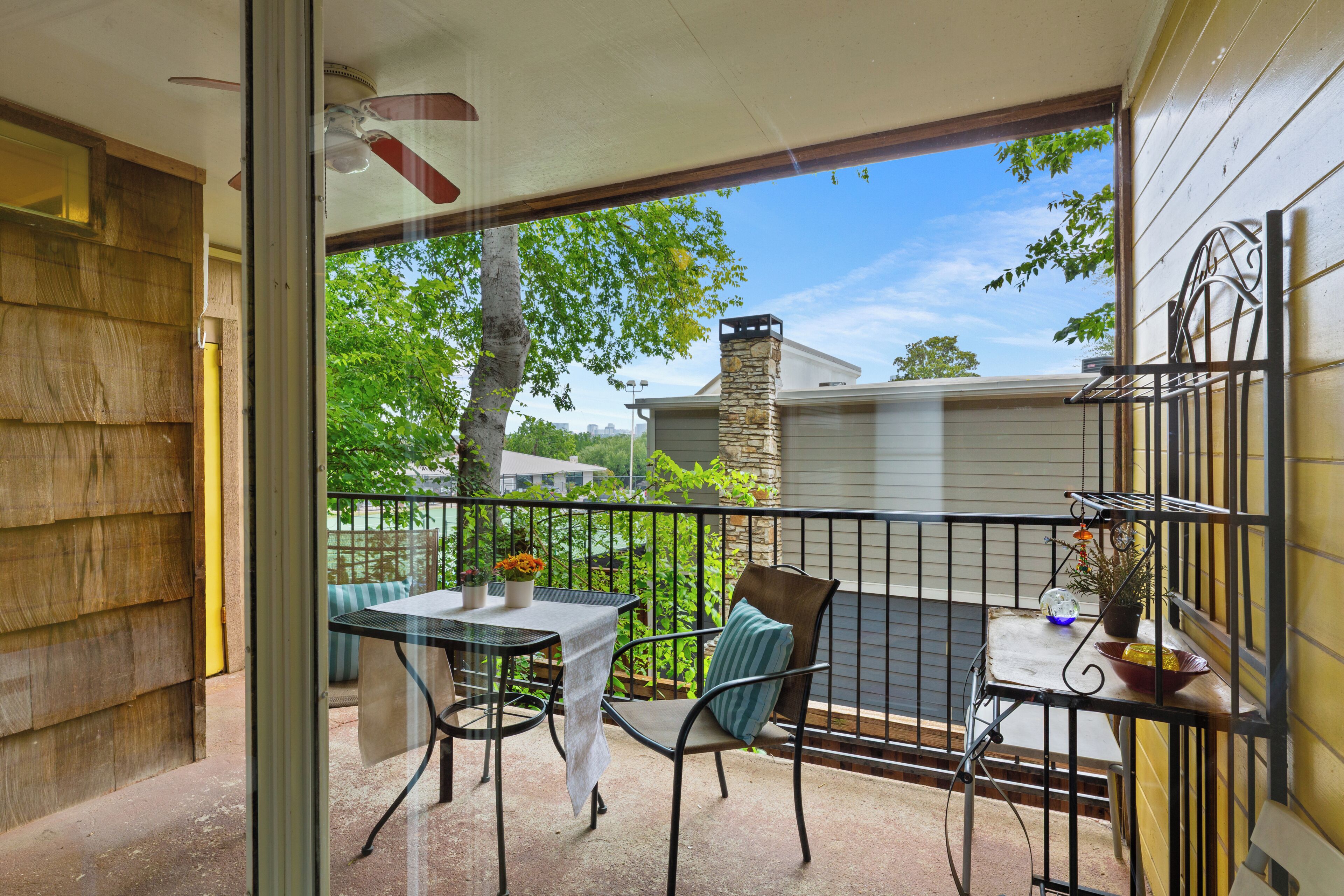 A balcony with a table and chairs, a potted plant, and a view of the surrounding area.