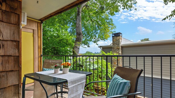 A balcony with a table and chairs, a view of trees and a building, and a stone chimney. - Walk to Zilker & Barton Springs / Old Austin Charm / Private Patio & Parking (Austin)