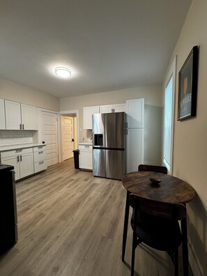 A kitchen with white cabinets, a stainless steel refrigerator, a wooden dining table, and a trash can. - 3-bedroom Minutes away from OSU.Short North.Downtown (Columbus)