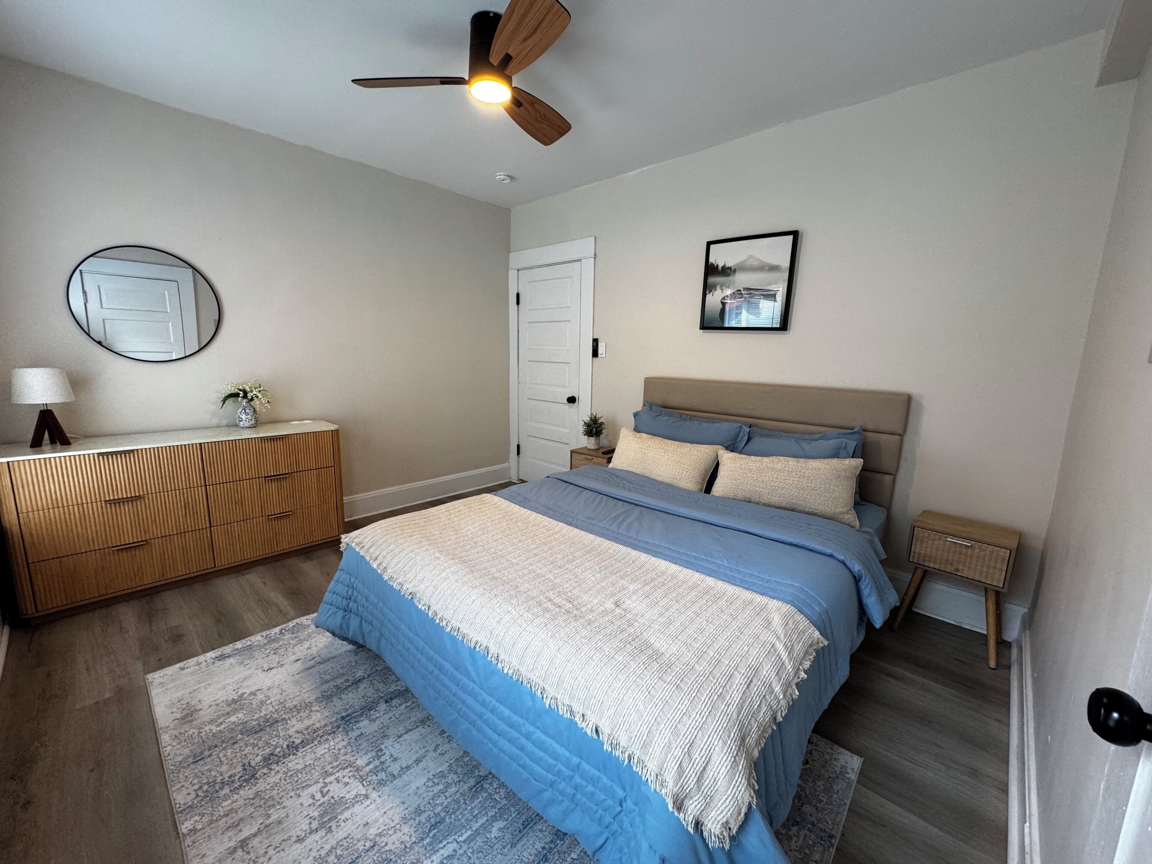 A bedroom with a bed, a dresser, a ceiling fan, a mirror, and a framed picture on the wall.