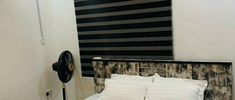 A hotel room with a bed, a wall-mounted air conditioner, a ceiling fan, and a window with blinds.