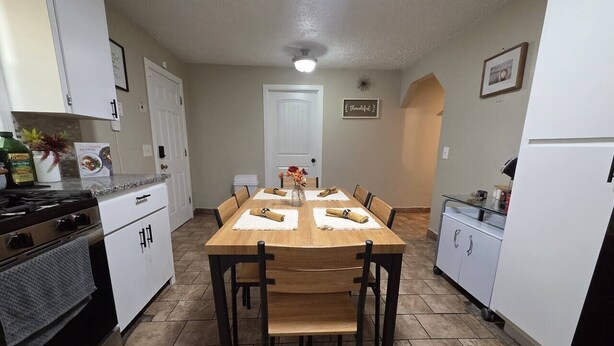 Uma cozinha com mesa de jantar, cadeiras, armários, fogão e geladeira.