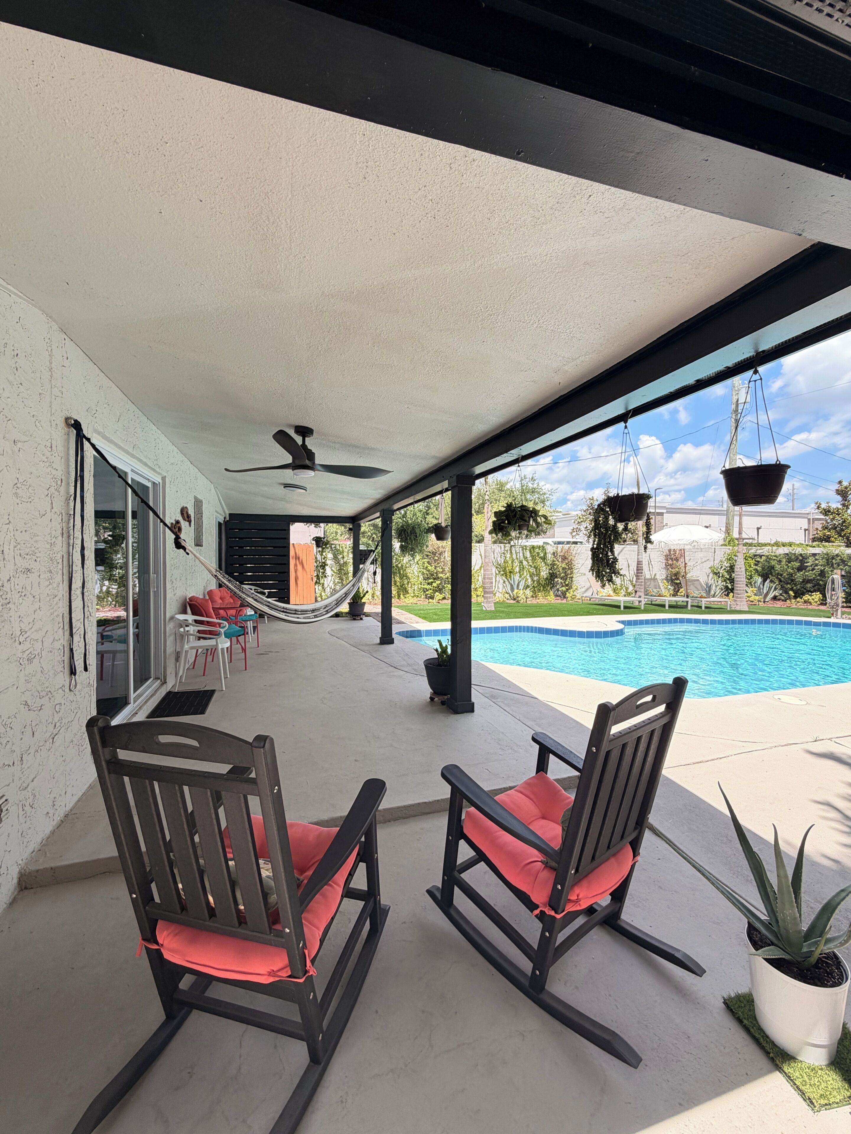 A covered patio with two rocking chairs, a pool, and a view of a residential area.