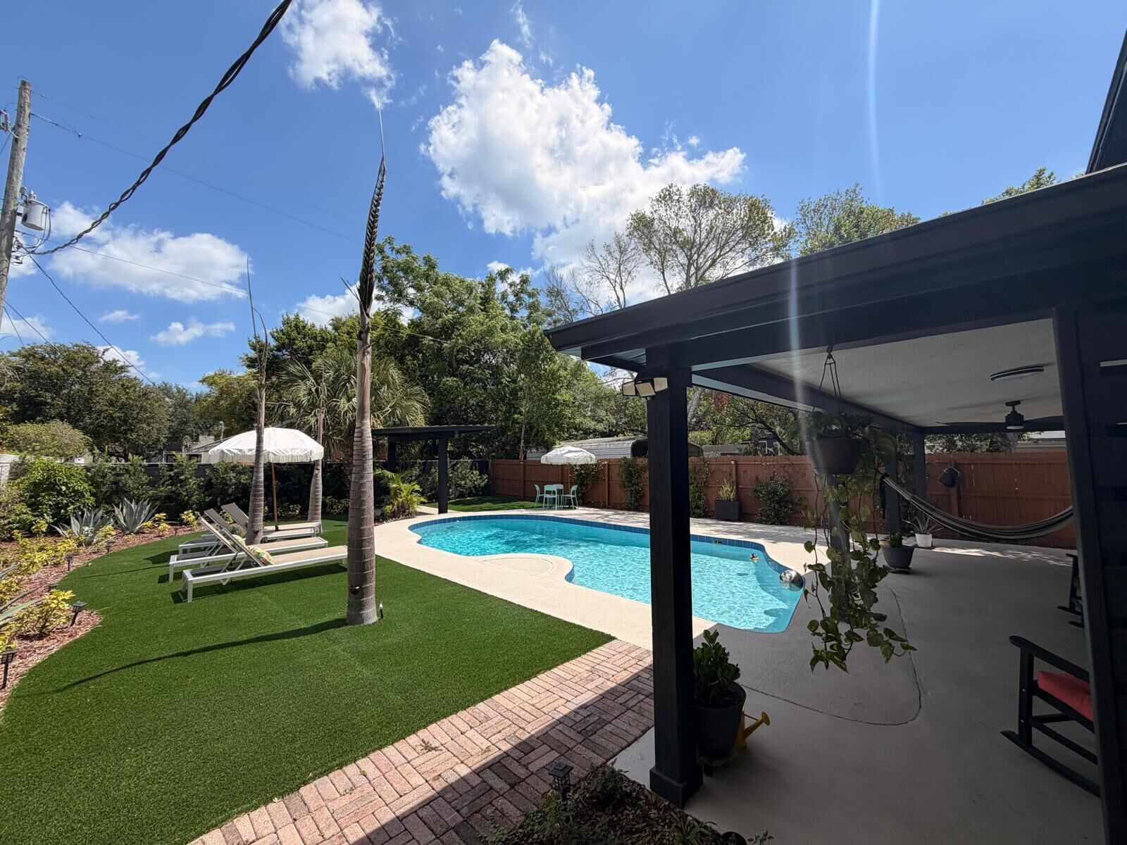 A backyard with a swimming pool, a covered patio, and a hammock.