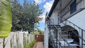 A brick pathway leading to a staircase with metal railings, surrounded by greenery and a white wall. - Peaceful Poolside Retreat Near Orlando Health.  Resort Style Amenities Workspace (Orlando)