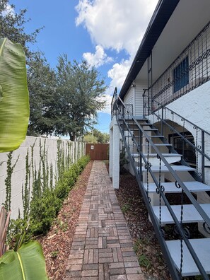A brick pathway leading to a staircase with metal railings, surrounded by greenery and a white wall. - Peaceful Poolside Retreat Near Orlando Health.  Resort Style Amenities Workspace (Orlando)