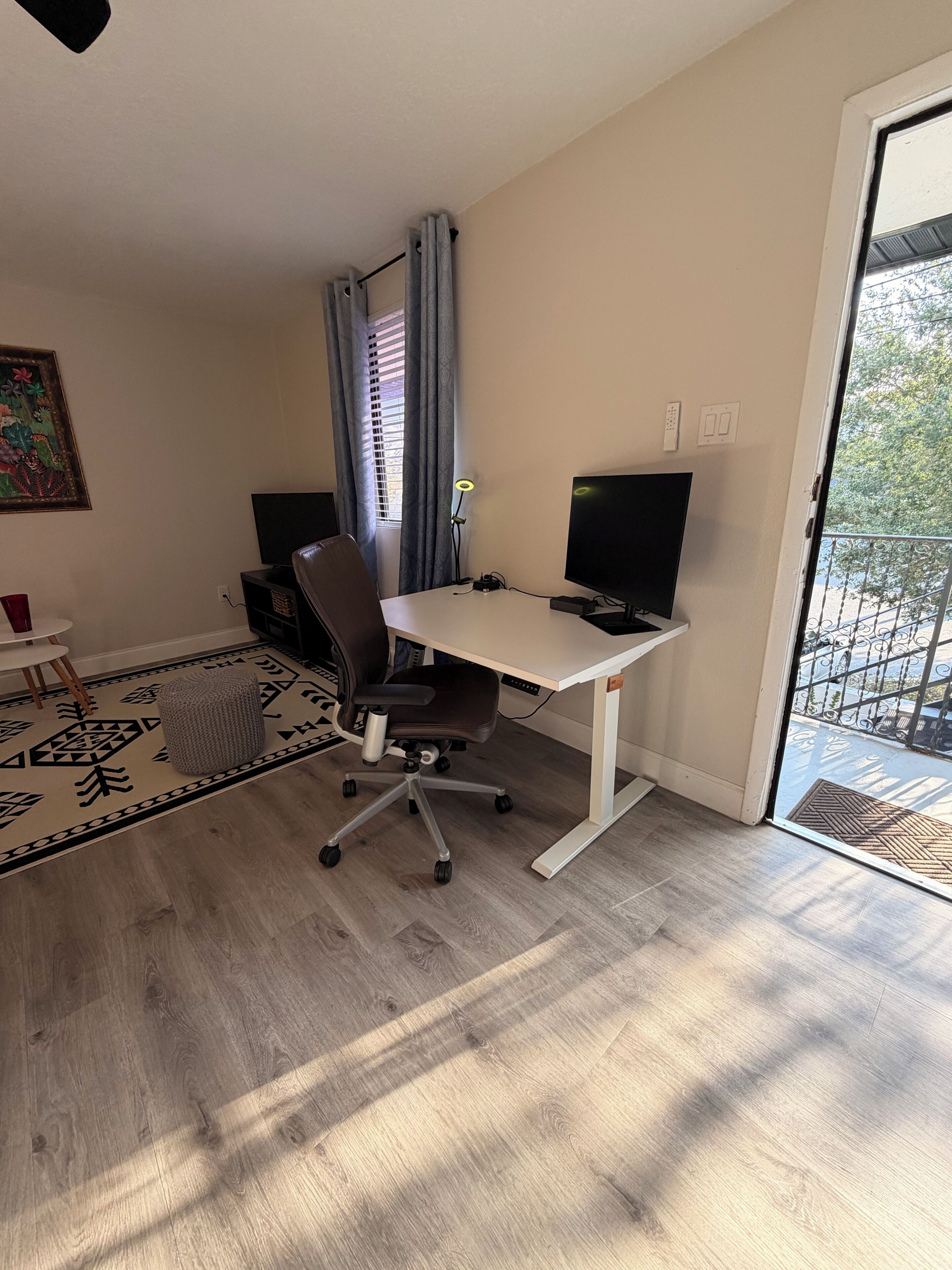 A room with a desk, chair, computer, and a view through a door.