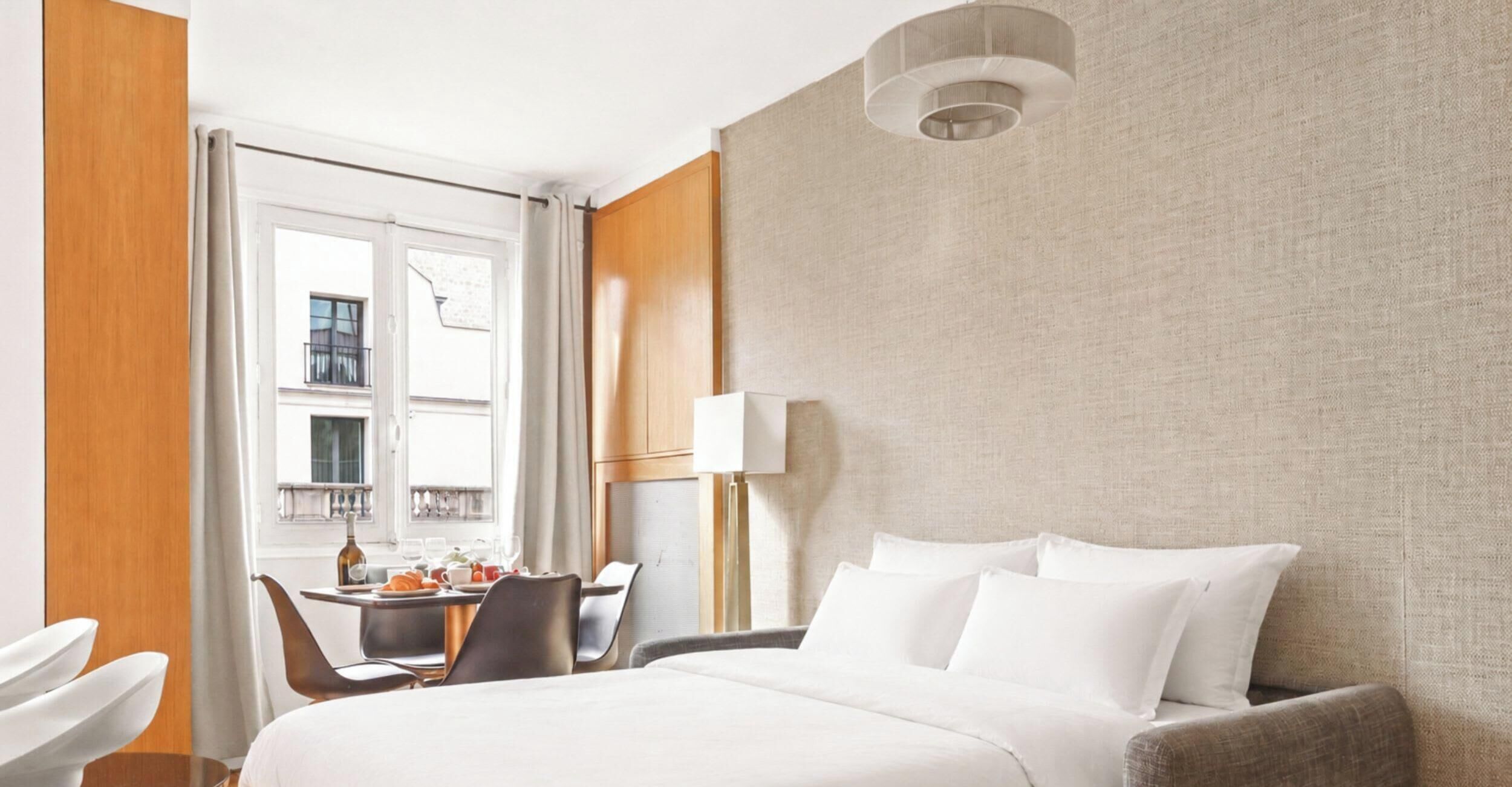 A hotel room with a bed, a desk, a chair, and a window with curtains.